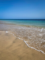 Sandy Atlantic Ocean beach with soft waves against turquoise and blue water and blue sky