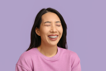 Young Asian woman laughing on lilac background