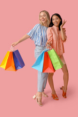 Beautiful young women with shopping bags on pink background