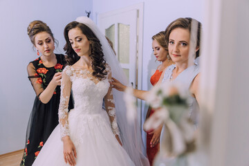 A bride is getting ready for her wedding with the help of her bridesmaids. The bride is wearing a...