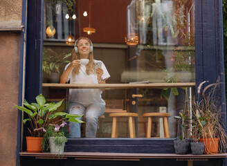 A woman smiling while sipping coffee at a window table in a trendy caf