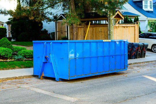 A blue roll-off construction dumpster outside a residential renovation project in an older neighourhood. shot in toronto in the fall	