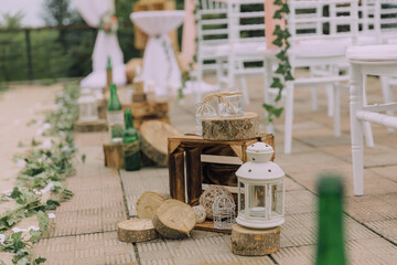 A wooden walkway with a variety of items, including bottles, chairs, and lanterns. Scene is rustic and natural, with the wooden crates and logs adding to the overall atmosphere