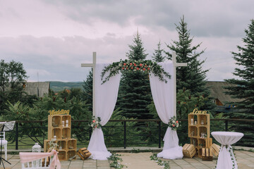 A wedding ceremony is taking place in a beautiful outdoor setting with a white archway and a white canopy. The archway is decorated with flowers and has the word 