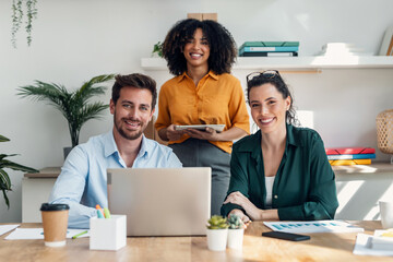 Casual young business people looking at camera while working in the new office.