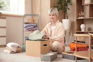 Beautiful young woman with cardboard box organizing clothes at home