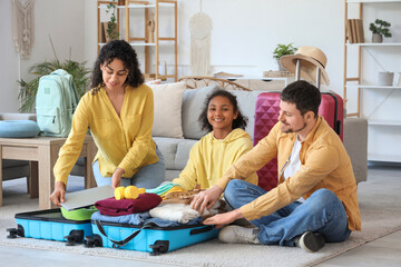 Happy family sitting on floor and packing suitcase for travel at home