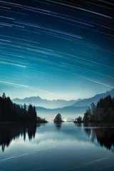 Night landscape with a beautiful lake in the Alps, village lights in front of the mountains, layers of mist and nice star trails in the dark blue sky
