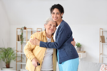 Young African-American female medical worker hugging elderly woman in nursing home