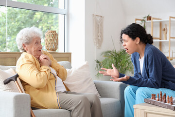 Young African-American female medical worker shouting at elderly woman in nursing home