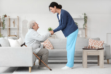 Young African-American female medical worker helping elderly woman in nursing home