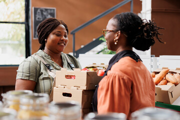 African American merchant provides organic fruits and vegetables at bio food market, promoting healthy, environmentally conscious lifestyle. Black women grasping crates of fresh nutritious produce.