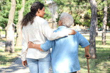 Young African-American female medical worker walking with elderly woman outdoors