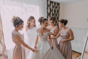 A bride and her bridesmaids are getting ready for the wedding. The bride is wearing a white dress...