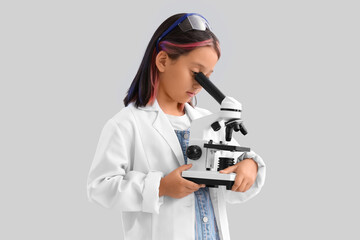 Cute little girl using microscope on grey background