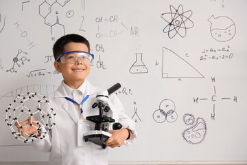 Cute little boy with molecular model and microscope in chemistry classroom