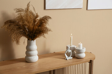 Burning candles with vase of pampas grass on dresser near beige wall in living room
