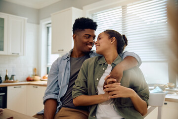 Happy mixed race couple embracing while relaxing in  kitchen.