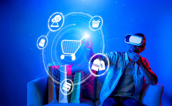 Happy man using VR headset and shopping online while sitting at sofa with shopping bags. Smart person looking at online market hologram and icon with neon background. Innovation technology. Deviation.