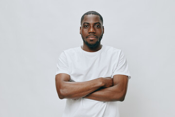 African man in a white t shirt with crossed arms, standing confidently against a light gray...