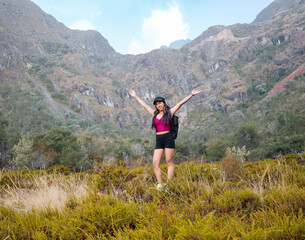 Fototapeta premium Hermosas montañas y mujer joven con short y mochila en el camino concepto de turismo. Paisaje con chica deportiva con top en la cima de la montaña, bosque, colinas, cielo blancos con nubes, Viaje,