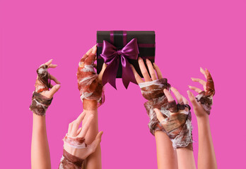 Female bandaged hands with Halloween gift on purple background