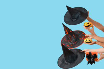 Female hands with Halloween gift, pumpkins and witch hats on blue background