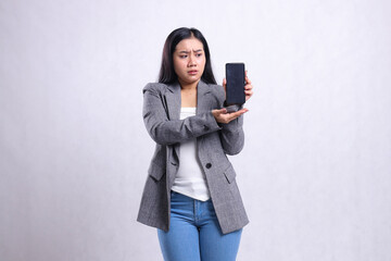 Fototapeta premium gesture young beautiful office ladies asia angry to mobile phone presenting holding showing cellphone screen wearing grey suit isolated on white background. for technology, lifestyle,promotion content