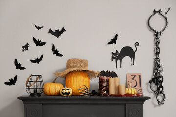 Fireplace with Halloween decorations near white wall with paper bats, cat and fetters