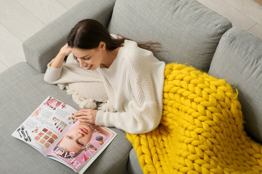 Beautiful young woman with warm yellow plaid reading magazine on sofa in living room