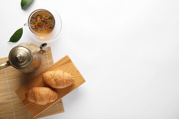 Composition with tea pot, bamboo mat and croissants on white background