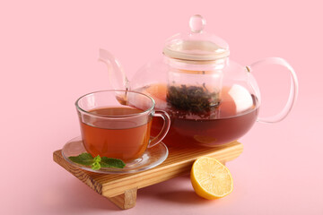 Beautiful composition with glass tea pot, lemon and wooden tray on pink background