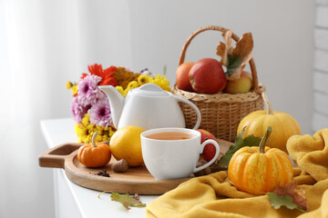 Tea pot, cup of tasty green tea, wooden tray, pumpkins, plaid and wooden tray on table in room