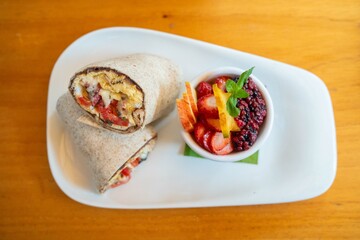 egg tomato and cheese burrito at organic breakfast cafe with a side of colorful fruits