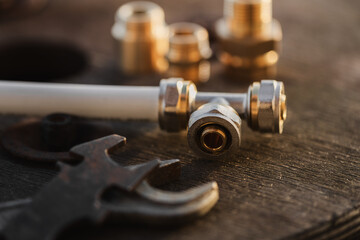 Brass plumbing fittings and PEX pipe fittings lying on an old wooden countertop, next to a tool,...