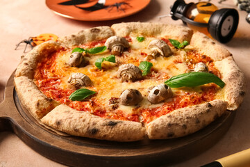 Wooden board of tasty pizza with mushrooms and basil for Halloween celebration on beige background