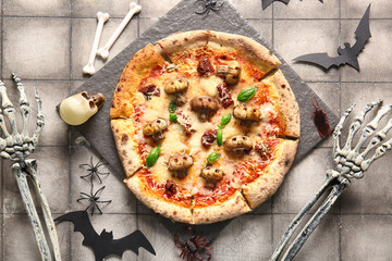 Board of tasty pizza with mushrooms, spiders, paper bats, bones and skeleton hands for Halloween celebration on grey tile background