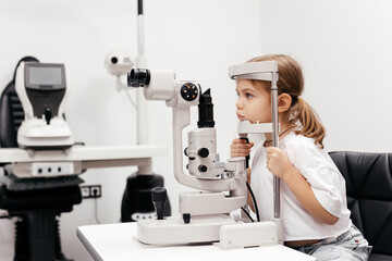 In a modern ophthalmology clinic, an ophthalmologist checks a little girl's vision using a...