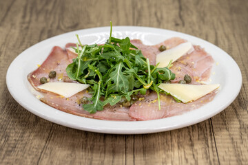 Italian appetizer with raw tuna with slices of parmesan cheese, arugula, and capers arranged on a plate