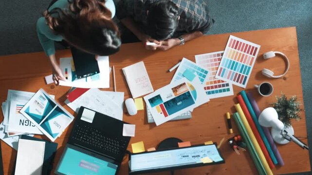 Top down view of smart designer helping manager choosing color from colored palettes. Aerial view of businessman working together and planning together while looking at logo from laptop. Symposium.