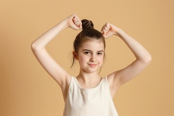 Fototapeta premium Cute teenage girl with developed muscles posing on beige background. She looks confident, cheerful. Her facial expression conveys sense of joy, happiness. Suitable for lifestyle, fashion content.