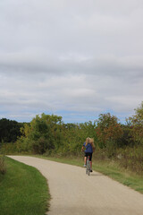 Fototapeta premium Woman with long red hair riding a bicycle on the Des Plaines River Trail in autumn at Old School Forest Preserve in Libertyville, Illinois