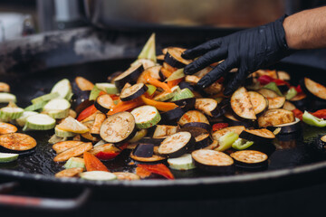 Food festival with street food stall kiosk, open-air outdoor fair market, assortment of different fried grilled barbecued vegetables, pepper, eggplant, zucchini, aubergine, cabbage on a large pan