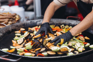 Food festival with street food stall kiosk, open-air outdoor fair market, assortment of different fried grilled barbecued vegetables, pepper, eggplant, zucchini, aubergine, cabbage on a large pan