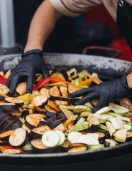 Food festival with street food stall kiosk, open-air outdoor fair market, assortment of different fried grilled barbecued vegetables, pepper, eggplant, zucchini, aubergine, cabbage on a large pan