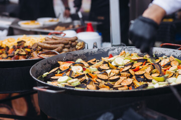 Food festival with street food stall kiosk, open-air outdoor fair market, assortment of different fried grilled barbecued vegetables, pepper, eggplant, zucchini, aubergine, cabbage on a large pan