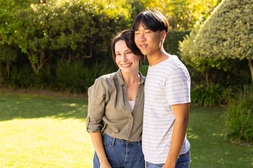 Obraz premium Smiling mother and teenage son embracing outdoors in sunny garden, enjoying quality time together
