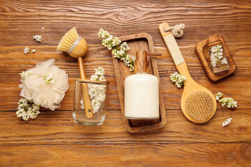 Soap dispenser with white lilac twigs, brushes and loofah on wooden background