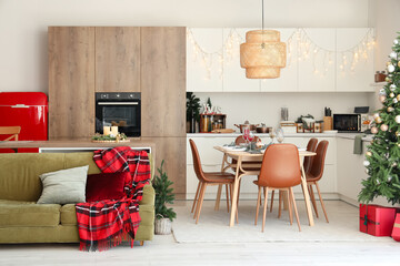 Interior of modern kitchen with Christmas decorations, green sofa and festive table setting