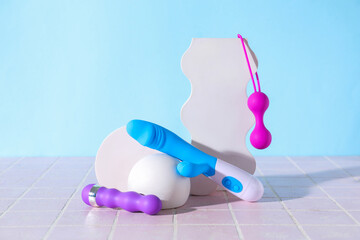 Decorative stands with different sex toys on pink tile near blue wall